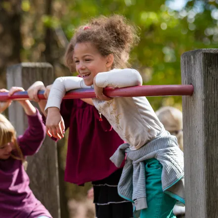 A young girl on top of a wooden play structure, smiling.